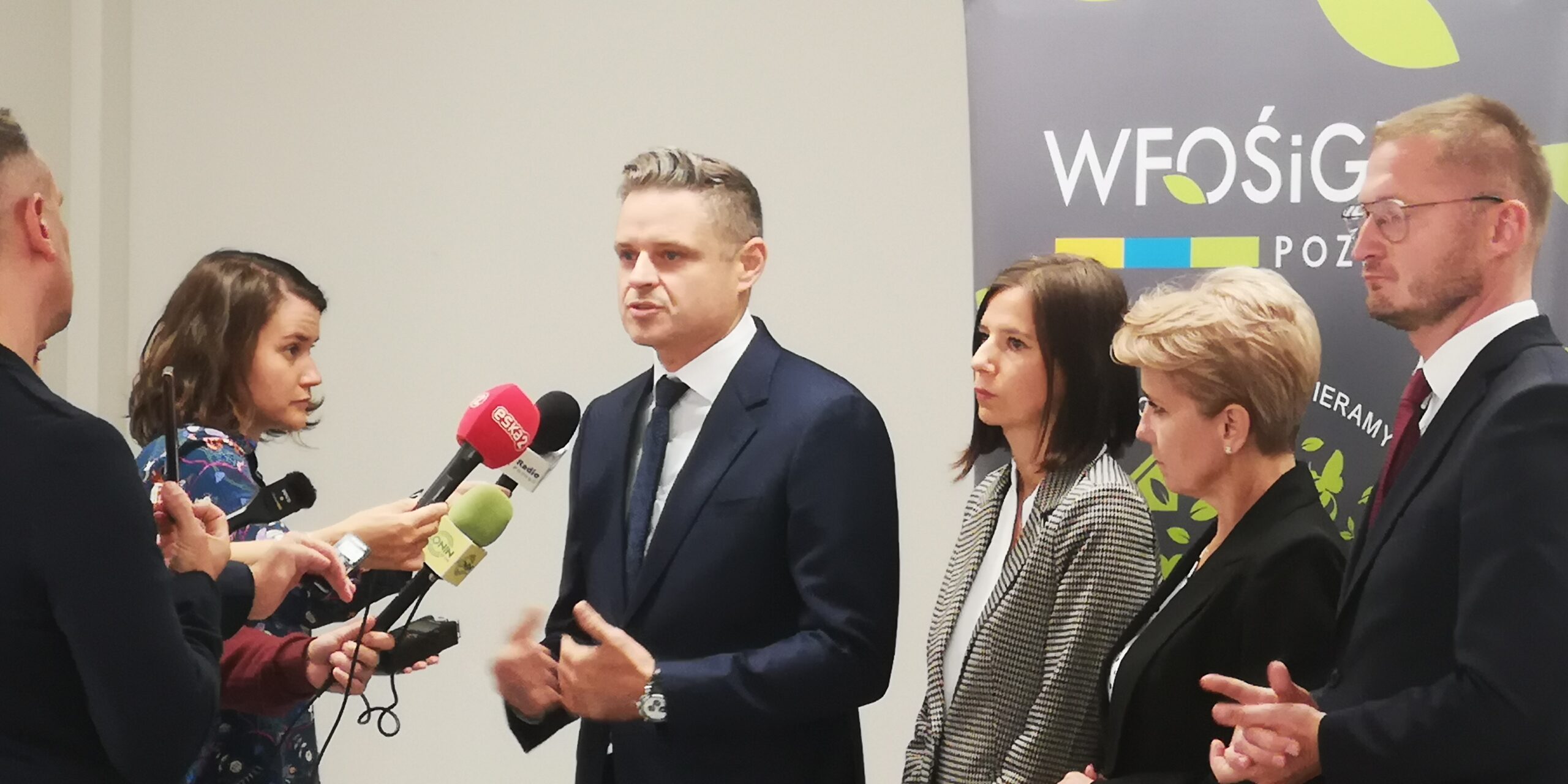 Kilka osób stoi przed kamerą i mikrofonem i udziela odpowiedzi napytania dziennikarzy.