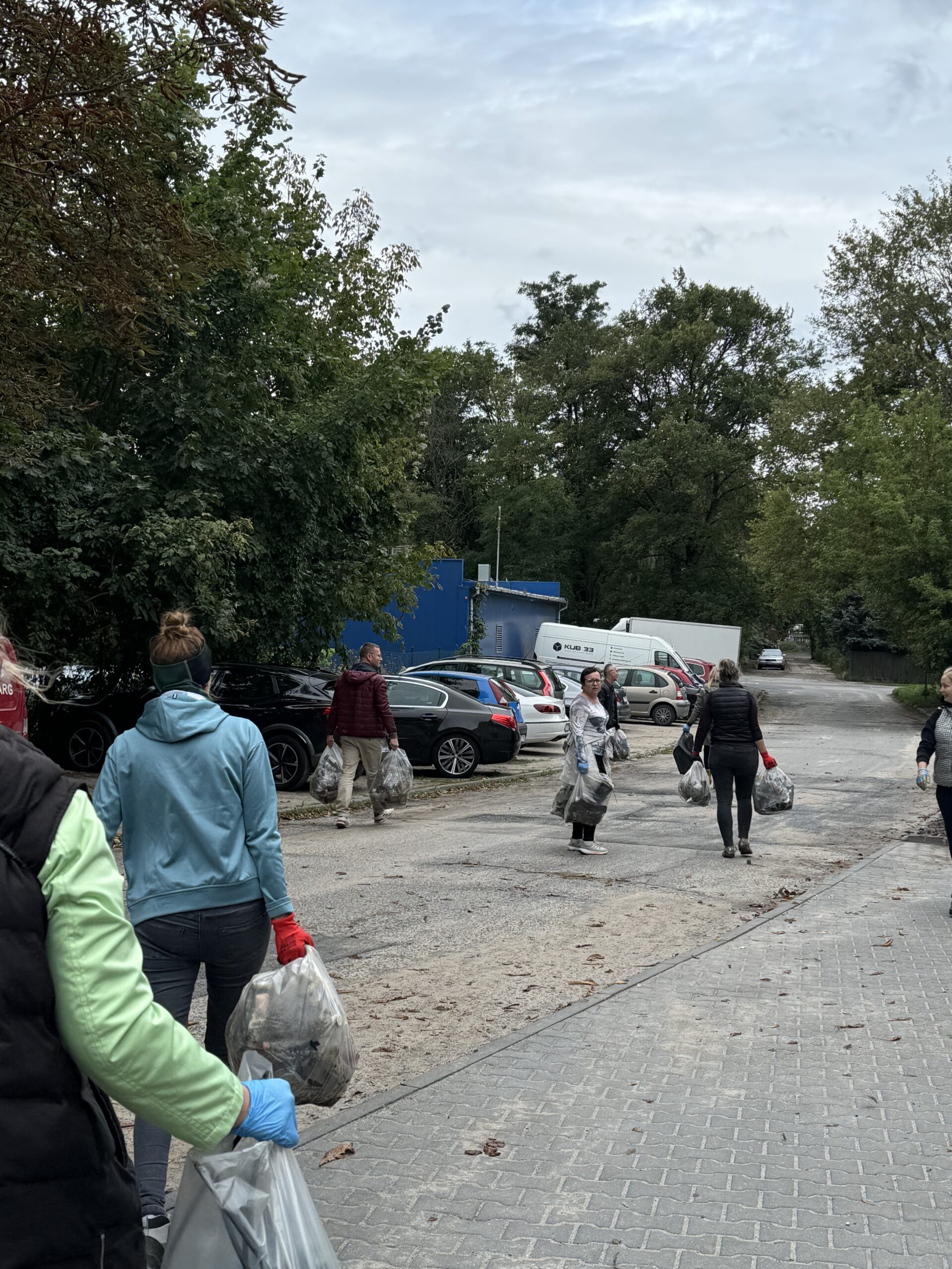 Sprzątanie worków z uprzątniętymi odpadami. Na zdjęciu widać 7 osób, które zanoszą pozbierane worki z odpadami.