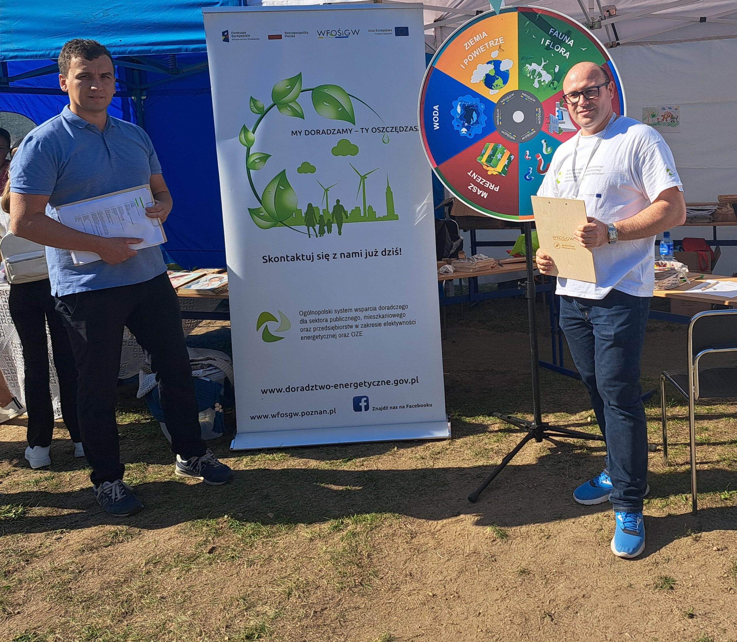 Dwie osoby stoją przed stoiskiem podczas festynu.