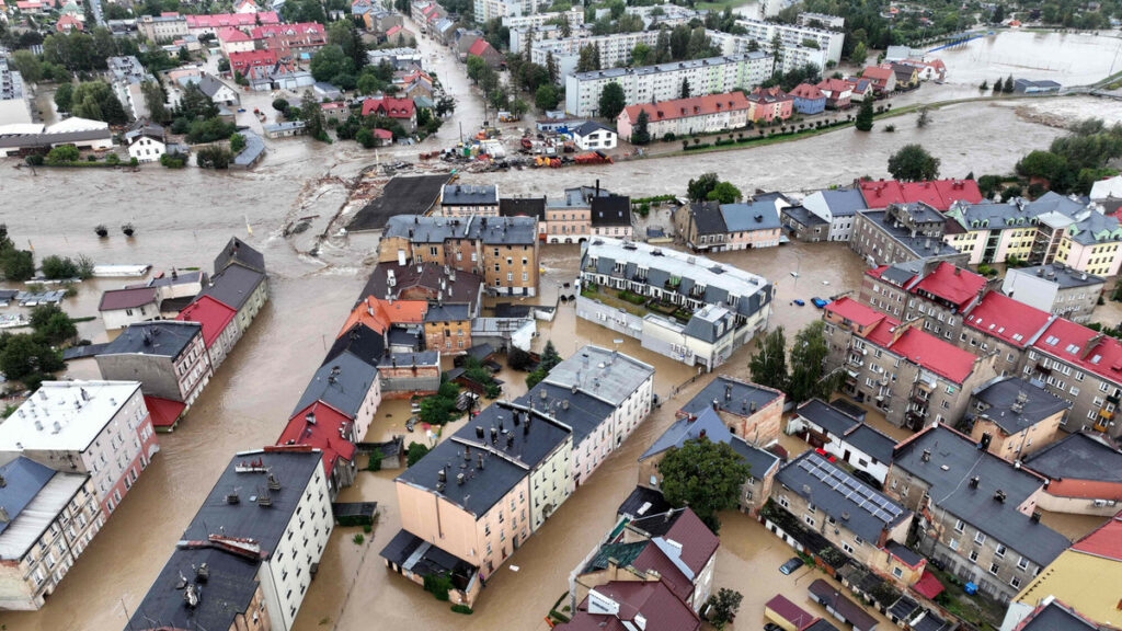 Zdjęcie przedstawia zalane miasto Głuchołazy, widać na nim stojącą wodę, zalane ulice, chodniki budynki i samochody.