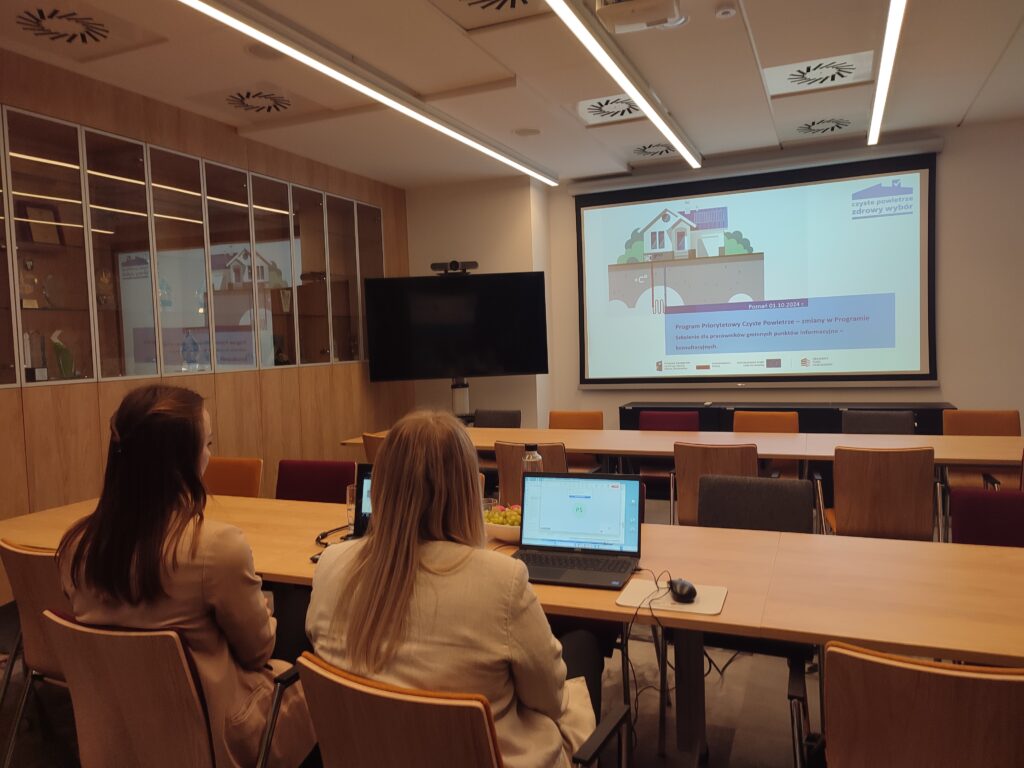 2 osoby siedzą przy stole naprzeciw wyświetlonej prezentacji i przeprowadzają szkolenie online.