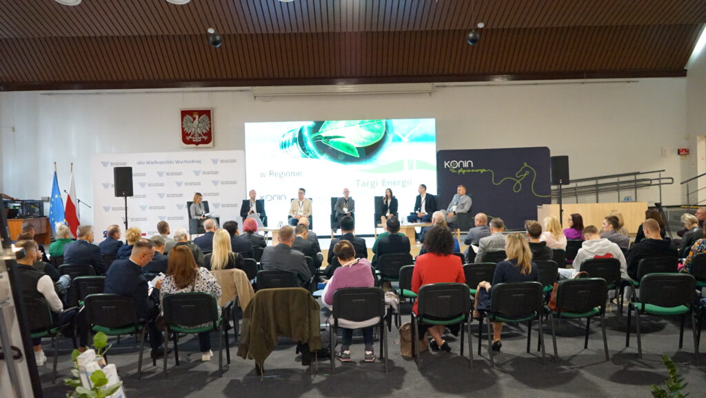 Zdjęcie przedstawia salę, w której obywał się panel dyskusyjny na temat współczesnej energetyki. Ludzie siedzą na krzesłach, a na podeście siedzą paneliści biorący udział w dyskusji.