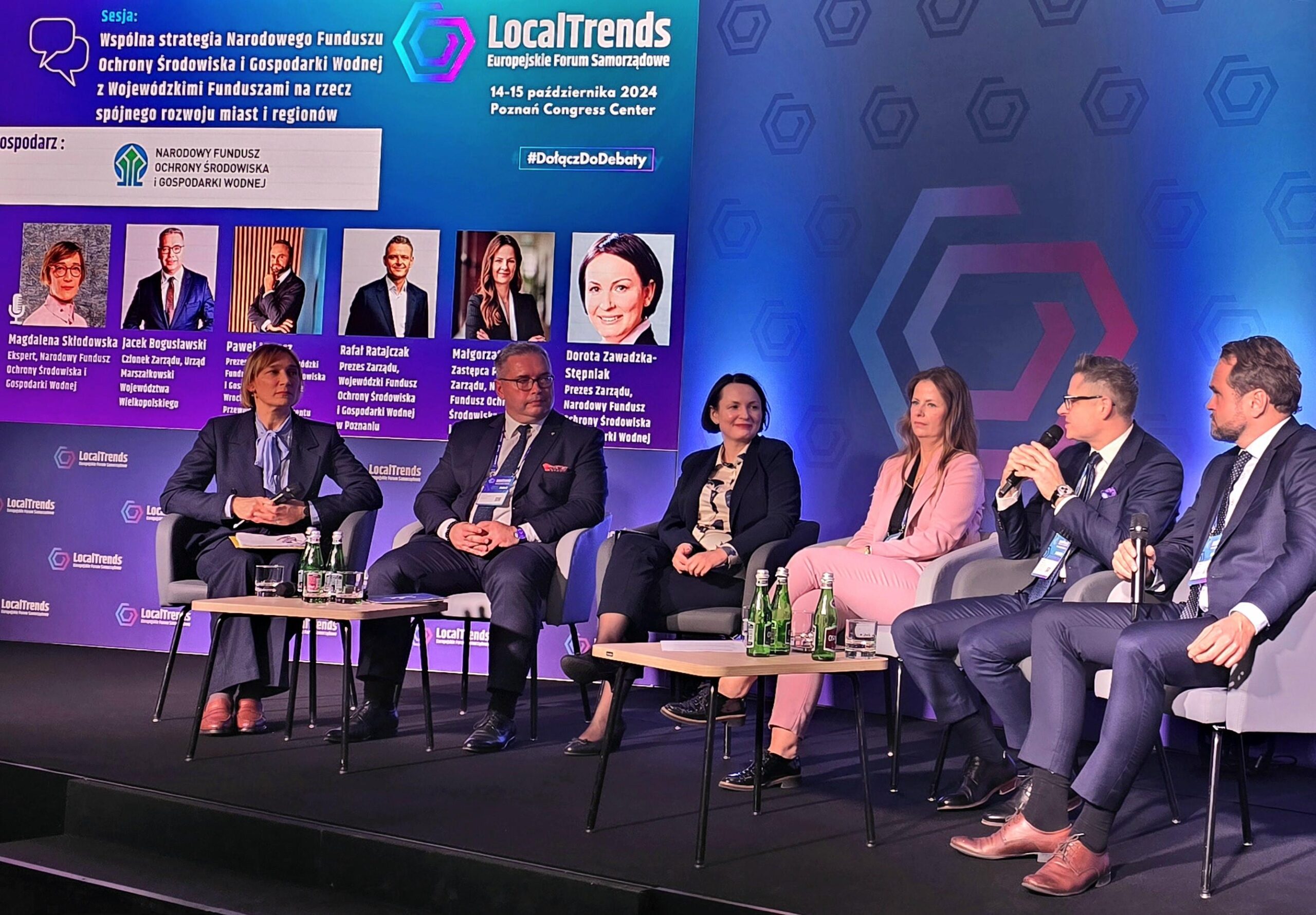 6 osób siedzi na krzesłach na zaaranżowanej podczas wydarzenia scenie, na tle ekranu, na którym wyświetlony jest temat debaty i rozmawia.