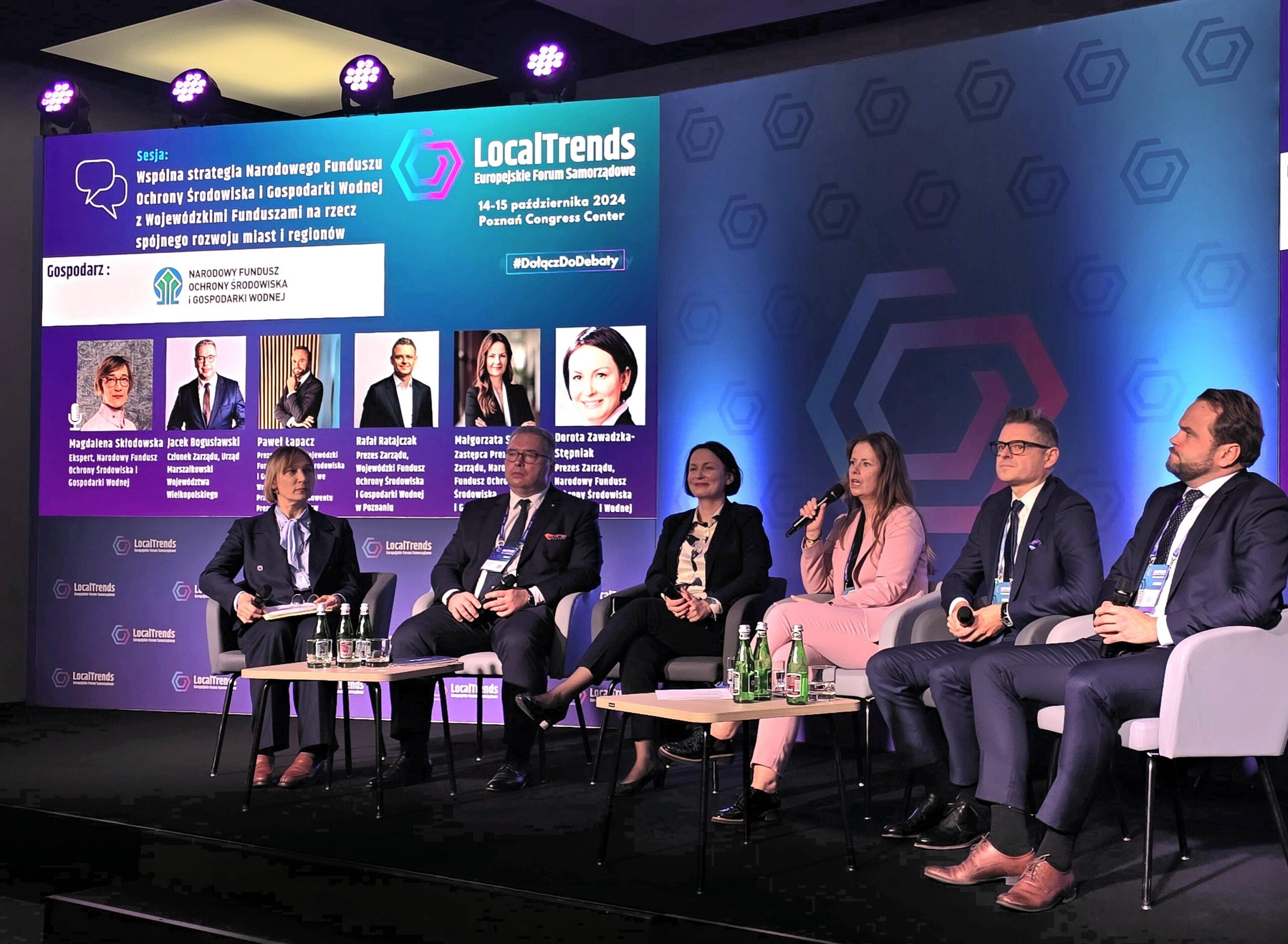 6 osób siedzi na krzesłach na zaaranżowanej podczas wydarzenia scenie, na tle ekranu, na którym wyświetlony jest temat debaty i rozmawia.