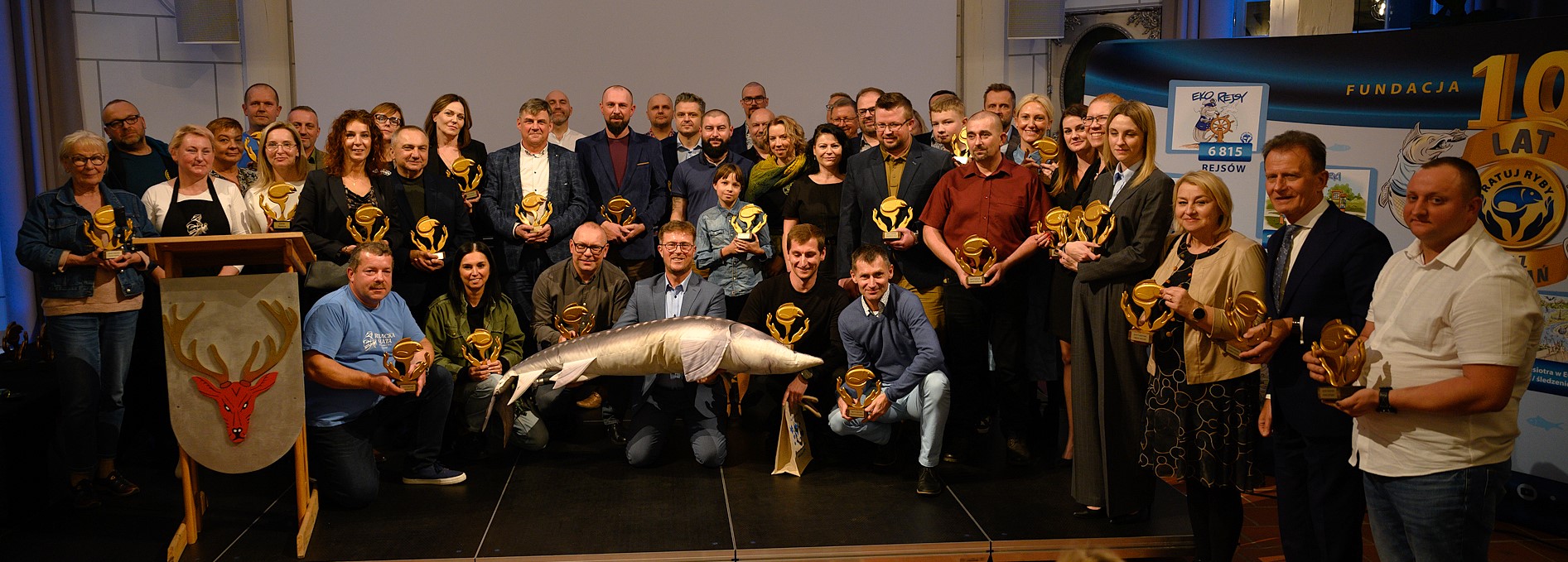 Zdjęcie przedstawia nagrodzone osoby pozujące do zdjęcia na scenie.