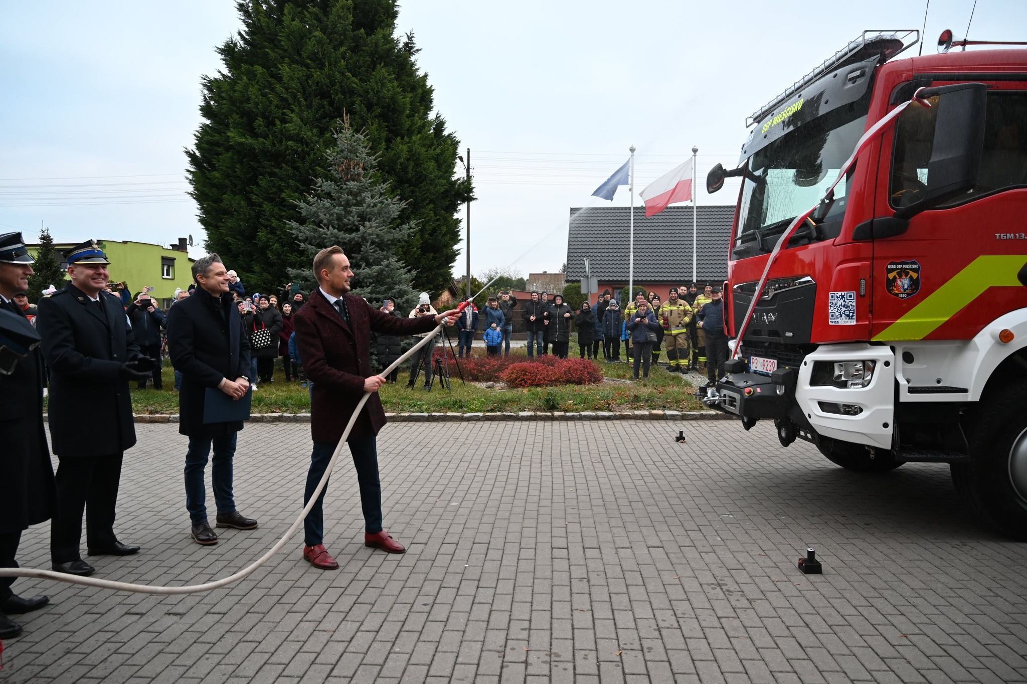 Zdjęcie przedstawia symboliczne oblanie wozu strażackiego z sikawki ręcznej.