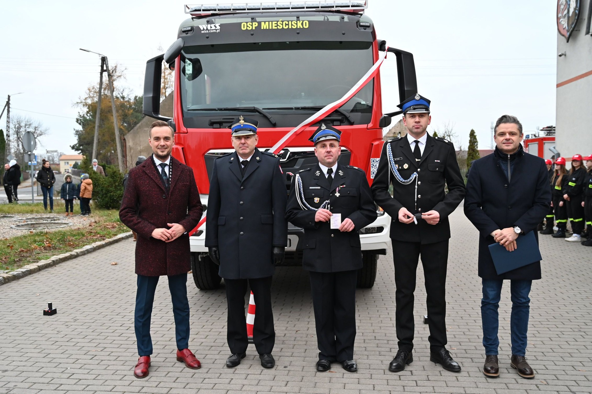 Zdjęcie przedstawia 5 osób stojących przed wozem strażackim.