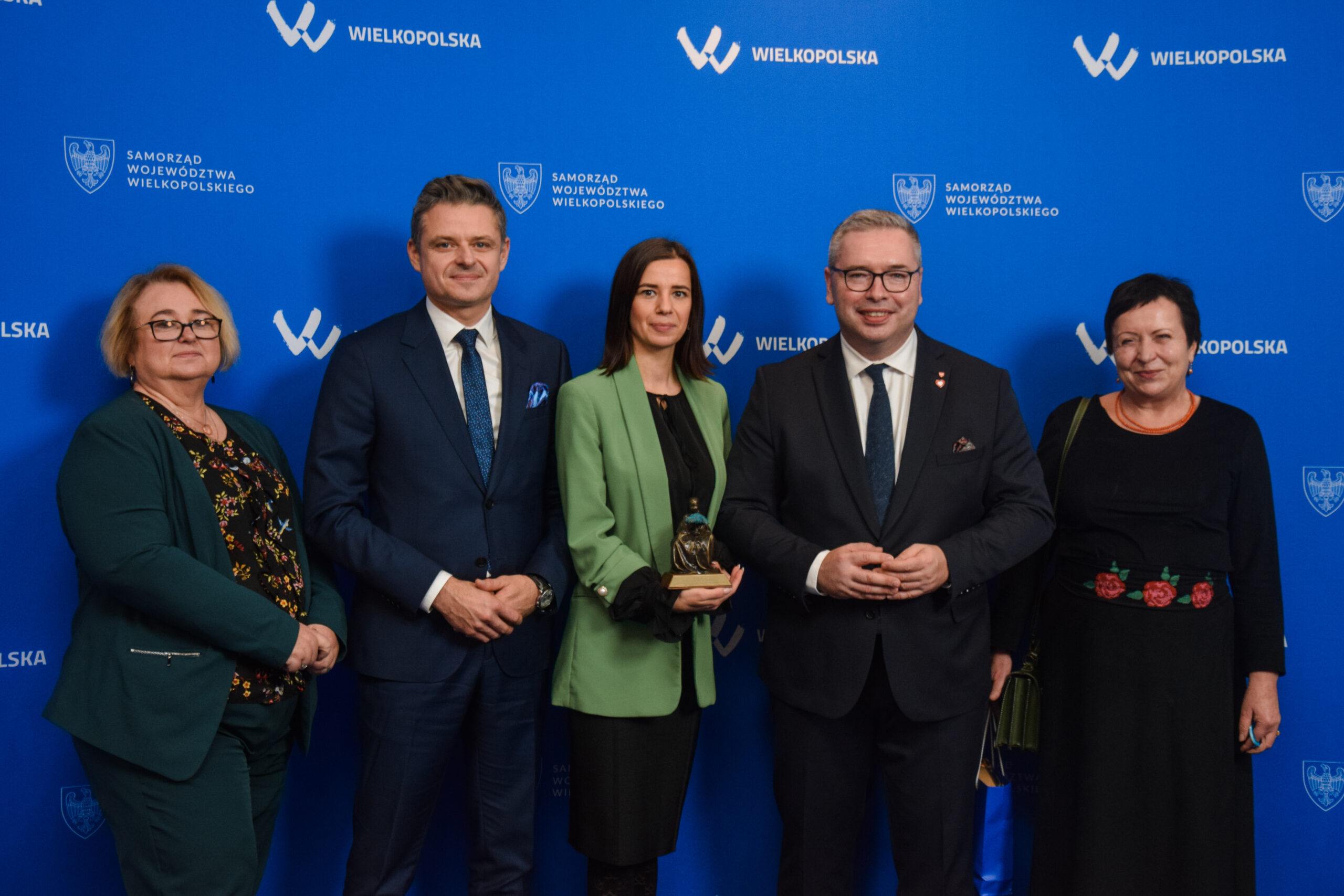 Na tle ścianki reklamowej stoi 5 osób i pozuje do zdjęcia.