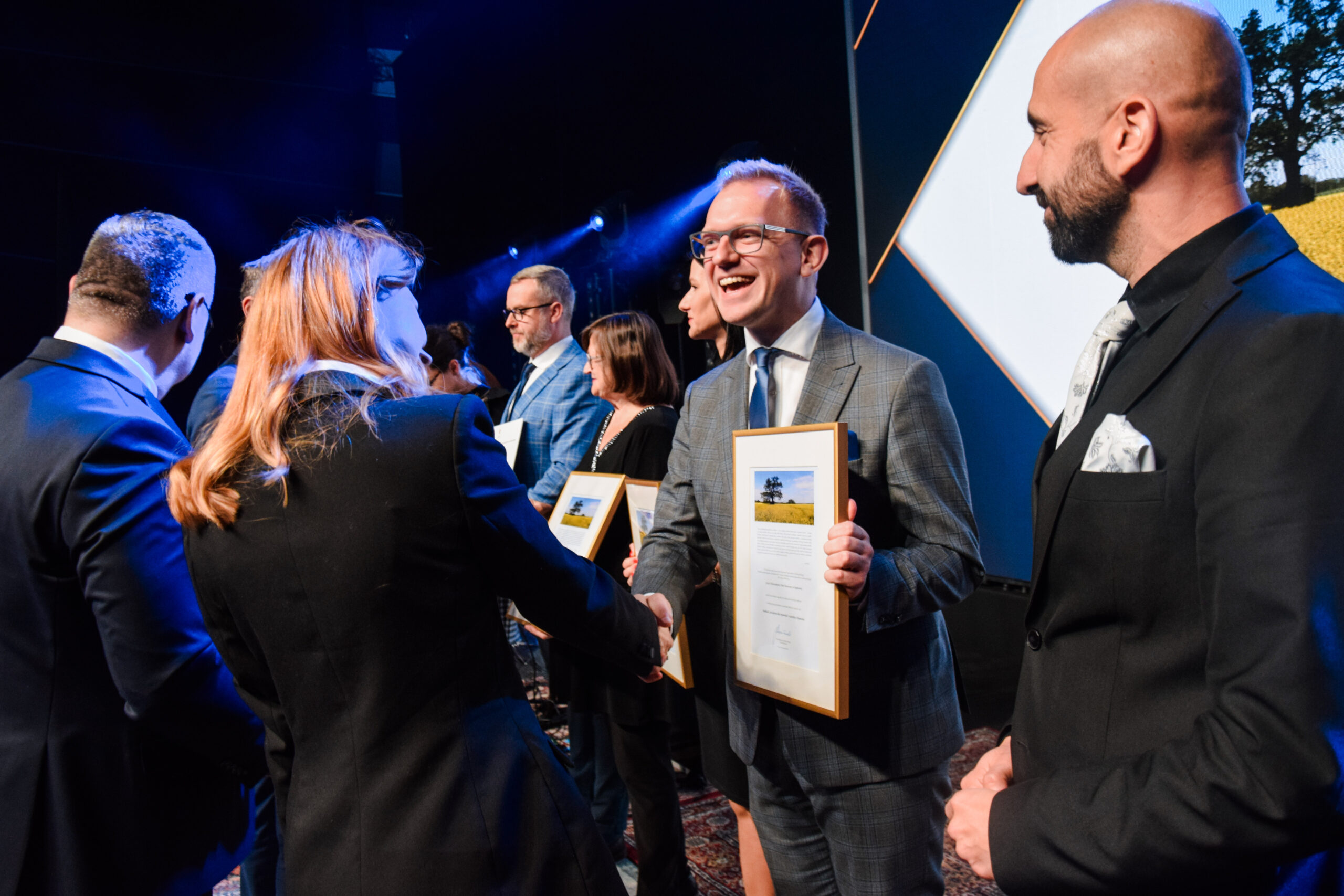 Na scenie stoi kilka osób i kolejne osoby wręczają nagrody oraz dyplomy.