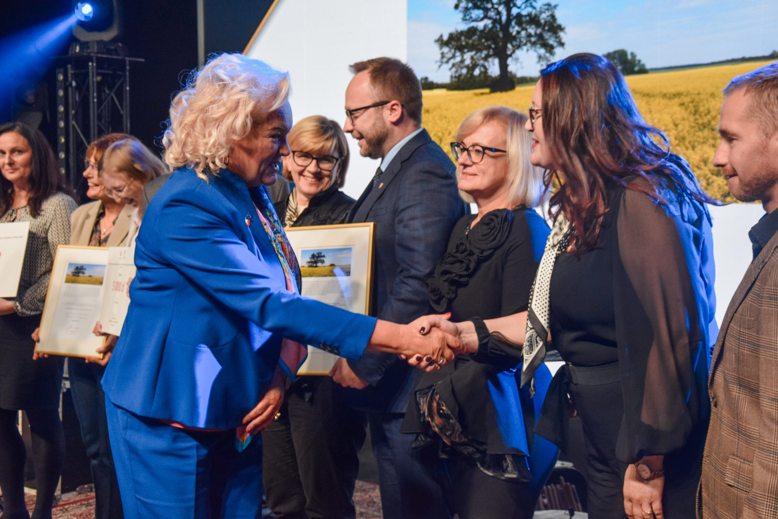 Na scenie stoi kilka osób i kolejne osoby wręczają nagrody oraz dyplomy.