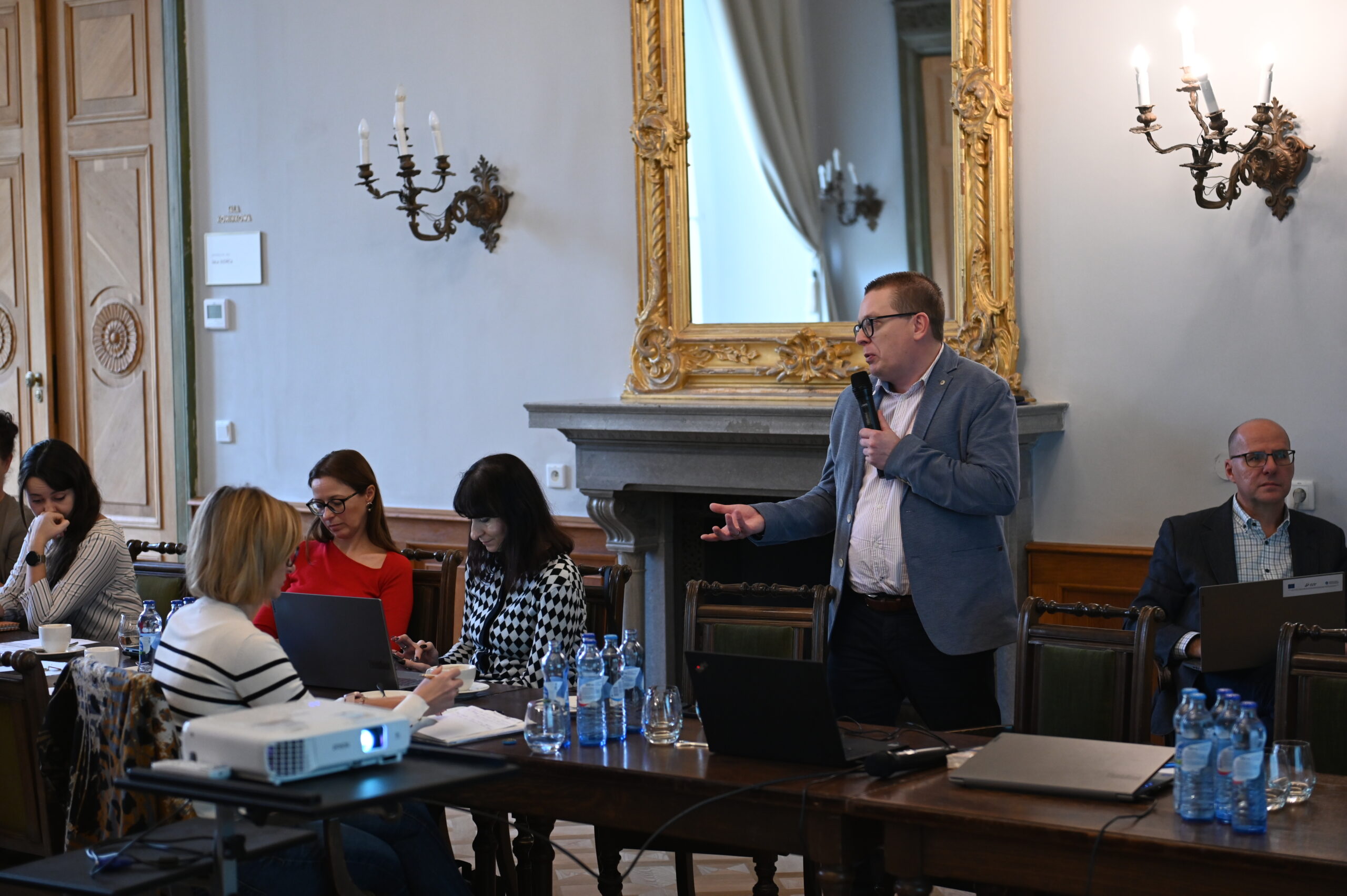 Na zdjęciu osoba prowadząca szkolenie, stoi i mówi do mikrofonu.