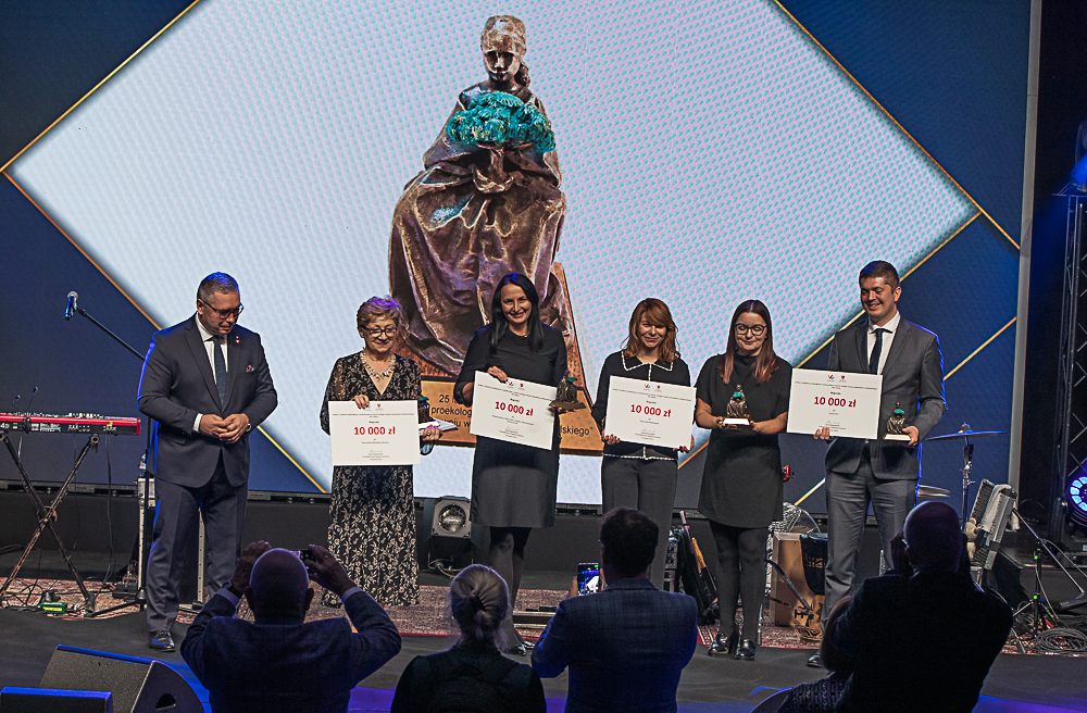 Na scenie stoi 6 osób z dyplomami i nagrodami i pozuje do zdjęcia.