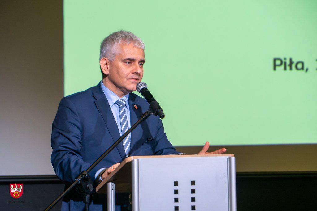 Jedna osoba stoi na scenie i przemawia zza mównicy.