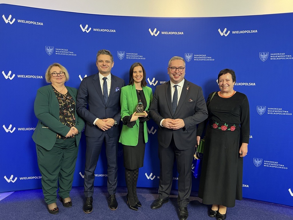 Na tle ścianki reklamowej stoi 5 osób i pozuje do zdjęcia.