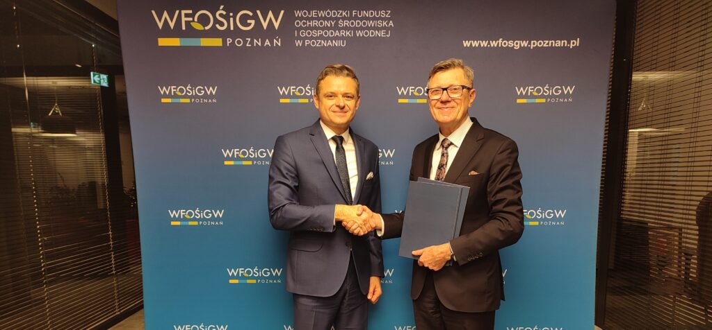 Dwie osoby stoją na tle ścianki reklamowej i podają sobie dłonie.