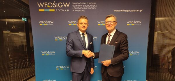 Dwie osoby stoją na tle ścianki reklamowej i podają sobie dłonie.