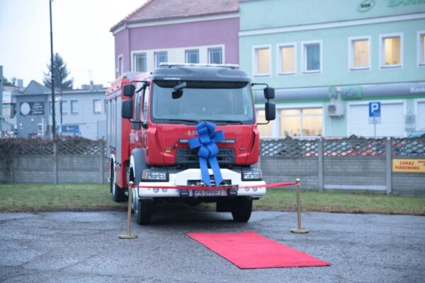 Zdjęcie przedstawia nowy wóz ratowniczo-gaśniczy, który stoi przodem i na przodzie ma założoną dużą niebieską kokardę.