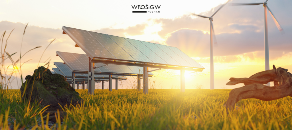 Zdjęcie przedstawia panele fotowoltaiczne oraz wiatraki na łące.