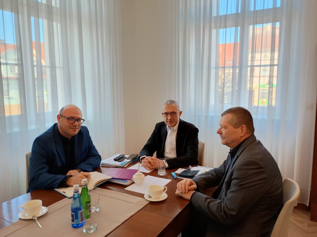 Na zdjęciu widzimy stół w gabinecie, przy którym siedzą 3 osoby i rozmawiają.