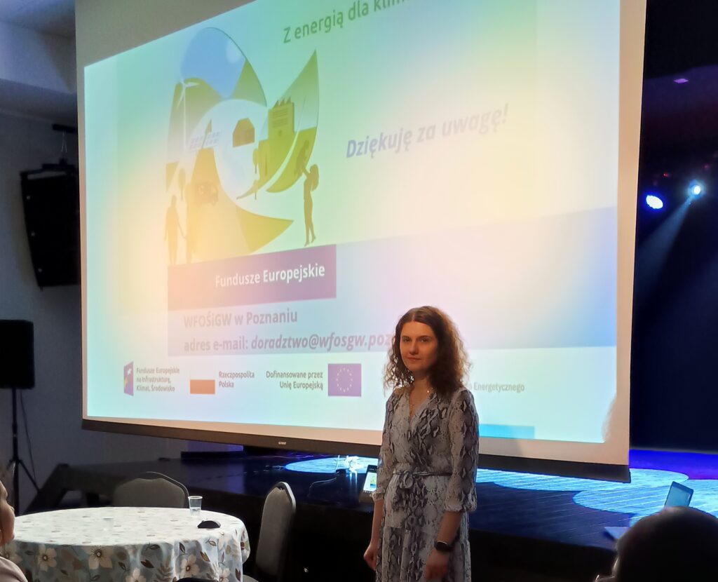 Na zdjęciu, na tle wyświetlanej prezentacji, stoi jedna osoba, która wygłasza prelekcję.