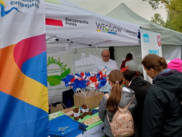 Zdjęcie przedstawia stoisko WFOŚiGW w Poznaniu na wydarzeniu plenerowym w Kłecku oraz ludzi odwiedzających stoisko.