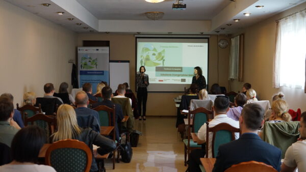 Zdjęcie przedstawia widok na salę, na której odbywa się szkolenie, na przodzie sali wyświetlona jest prezentacja, a osoby uczestniczące w szkoleniu siedzą na krzesłach.