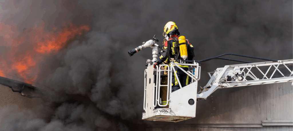 Zdjęcie przedstawia strażaka na wysięgniku, który walczy z dużym pożarem.