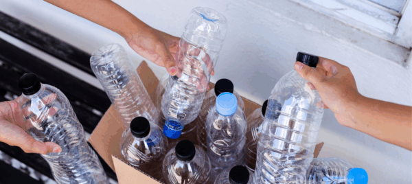 Na zdjęciu widzimy plastikowe butelki i ręce, które wkładają go do odpowiedniego pojemnika.