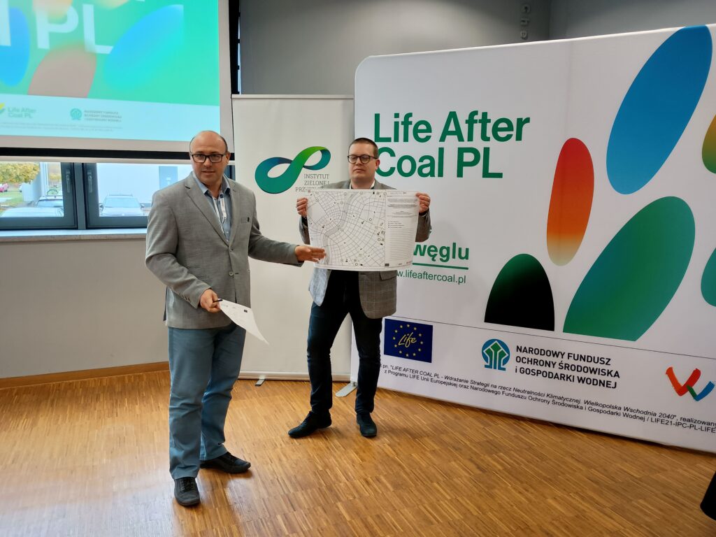 2 osoby stoją na tle ścianki reklamowej i prezentują.