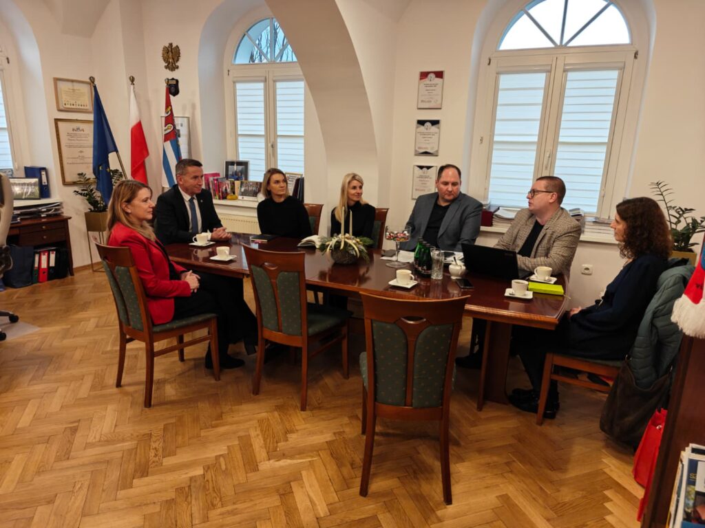 Przy stole w gabinecie siedzi 7 osób i rozmawiają.