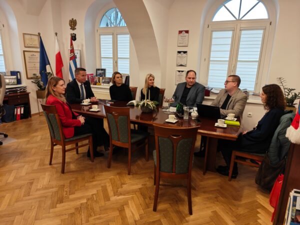 Przy stole w gabinecie siedzi 7 osób i rozmawiają.