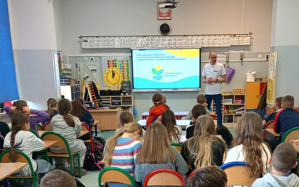 W klasie siedzą dzieci na krzesełkach, a na środku wyświetlana jest prezentacja i doradca klimatyczno-energetyczny omawia tematykę.