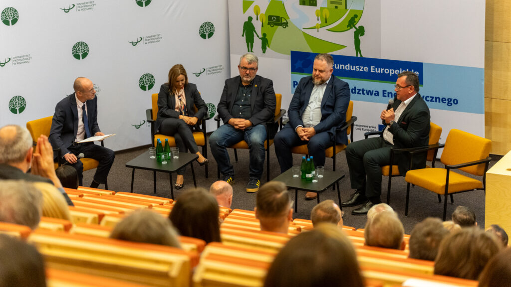 Pięć osób siedzi na fotelach na scenie i biorą udział w paneluy dyskusyjnym. Jedna z nich mówi do mikrofonu.