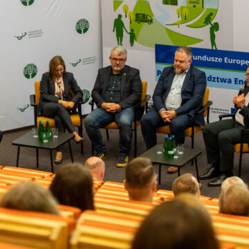 Pięć osób siedzi na fotelach na scenie i biorą udział w paneluy dyskusyjnym. Jedna z nich mówi do mikrofonu.